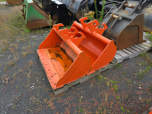 Bucket SSTA 42po orangé vue de 3/4 sur palette, godet d'excavation parmi d'autres accessoires