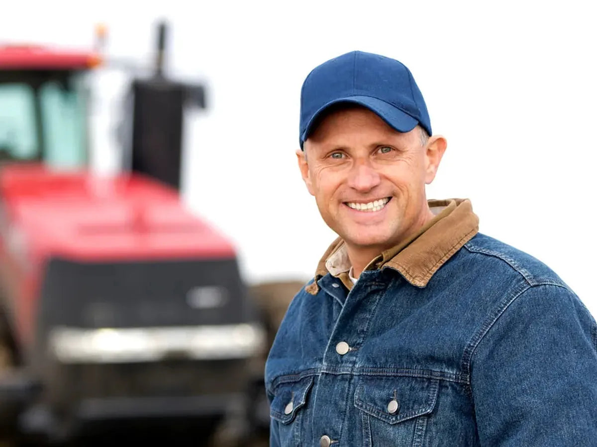 Agriculteur souriant à casquette bleue devant son tracteur, financement agricole Les Équipements Daigle
