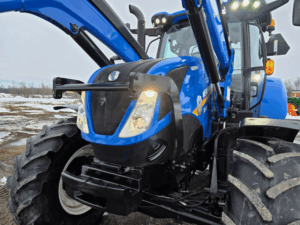 Face avant du New Holland T6.155 avec phares allumés et chargeur Quicke