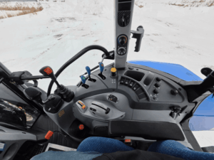 Vue depuis le siège opérateur du tracteur New Holland T5.95 usagé, année 2014 avec 3 147 heures. Tableau de bord clair et lisible, commandes accessibles et excellente visibilité vers l’avant pour l’utilisation du chargeur frontal STOLL. Poste de conduite ergonomique conçu pour le confort et la précision lors des travaux agricoles, de manutention et de déneigement. Tracteur prêt à travailler, disponible chez Les Équipements Daigle au Québec.