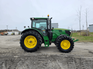 Full profile of a John Deere 6155R tractor in an equipment yard.