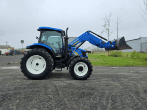 Side profile of the blue New Holland T6020 tractor with loader bucket raised.