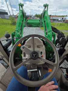 Operator's view from inside a John Deere 6110M tractor equipped with a front loader.
